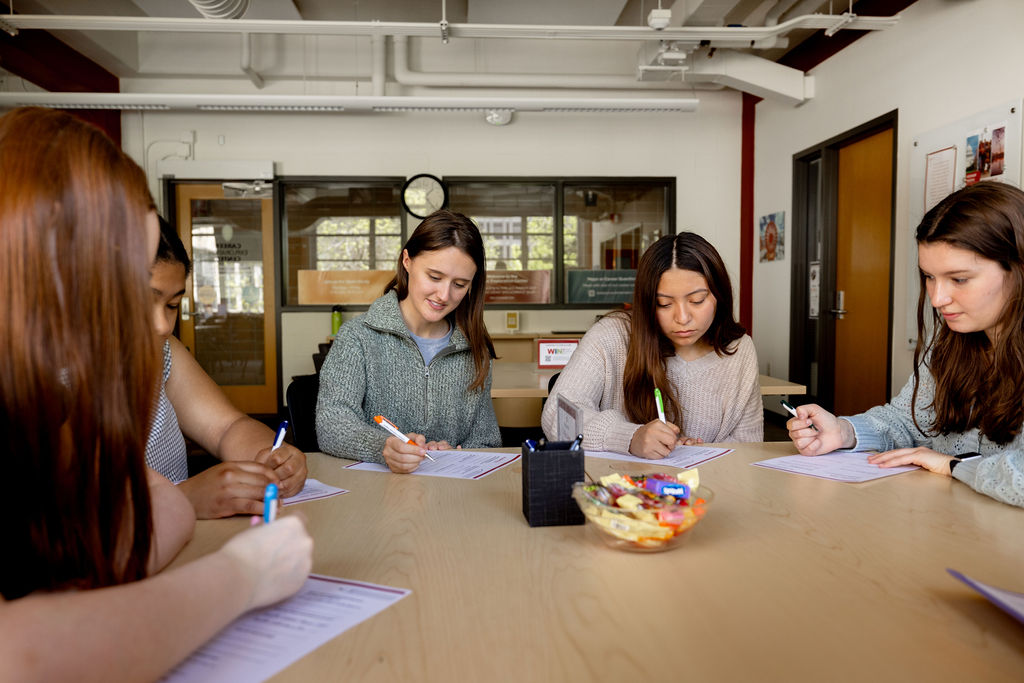 Group of students at a table writing on sheets of paper.