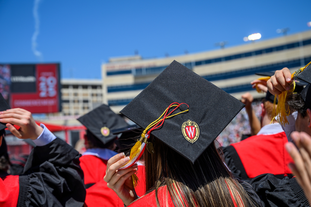 Student facing away from the camera wearing a graduation cap with a red W and tassles