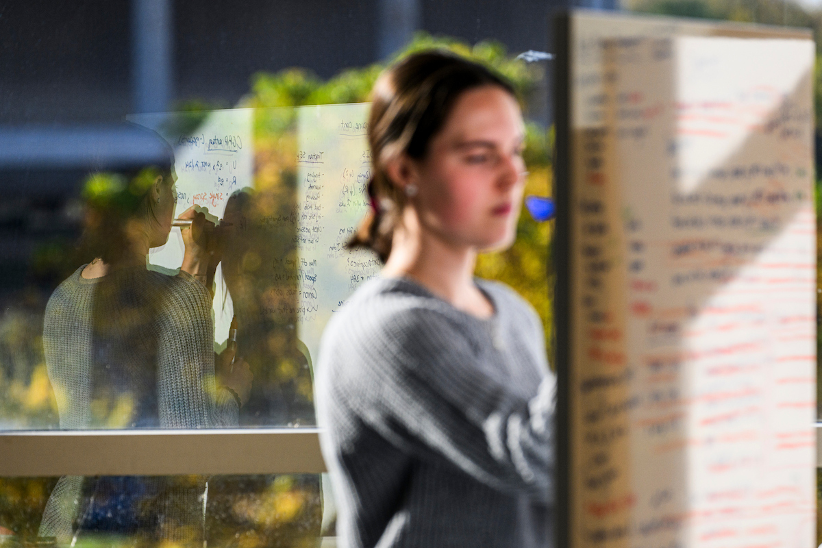 Student writing on a white board with her reflection in the background