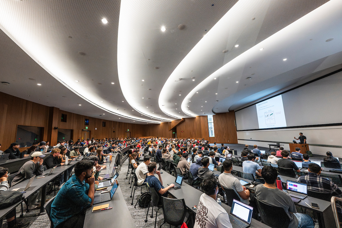Students sitting in a lecture lecture hall looking at a screen at the front of the room