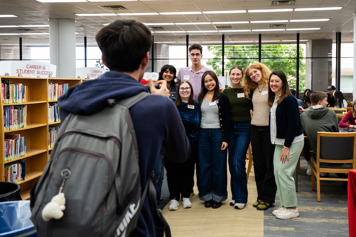 Student facing away from the camera taking a photo on their phone of a group of students looking at the camera