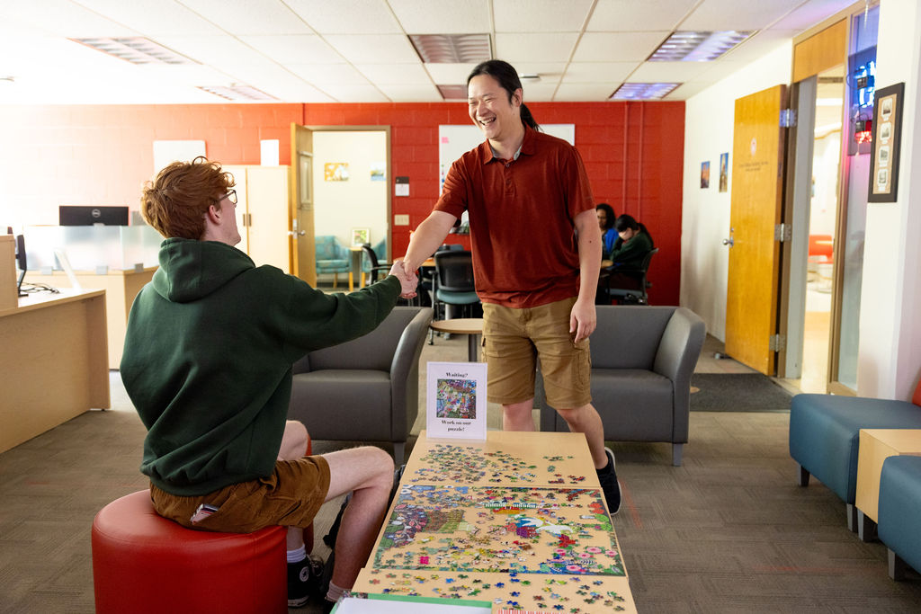Advisor shaking hands with a student who is sitting on a red stool in front of a puzzle