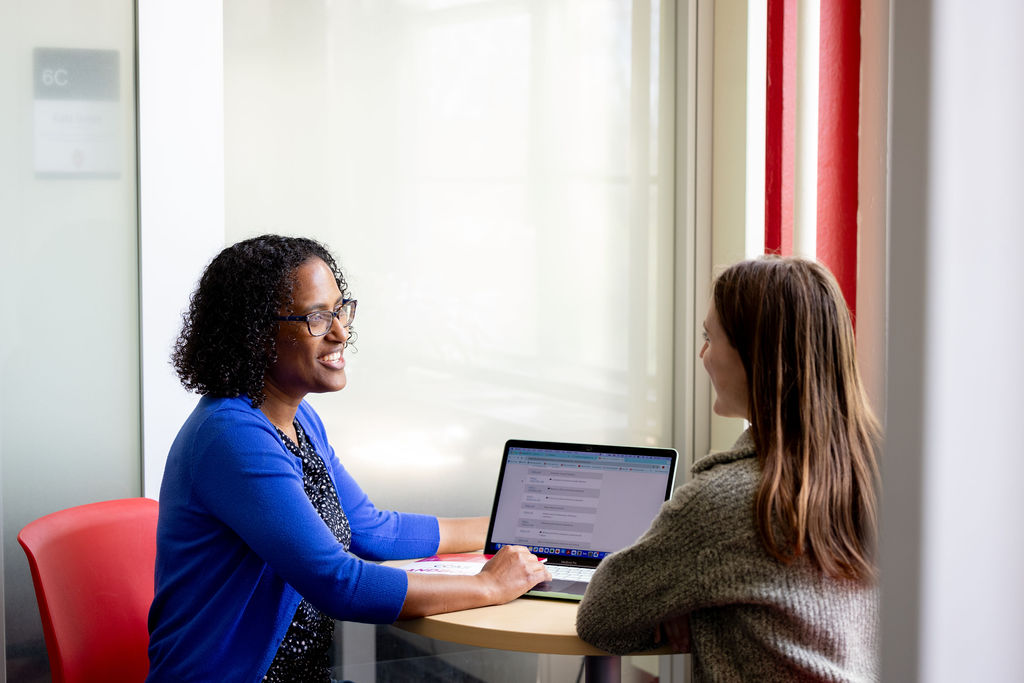 Advisor and student sitting together at a table with a computer between them