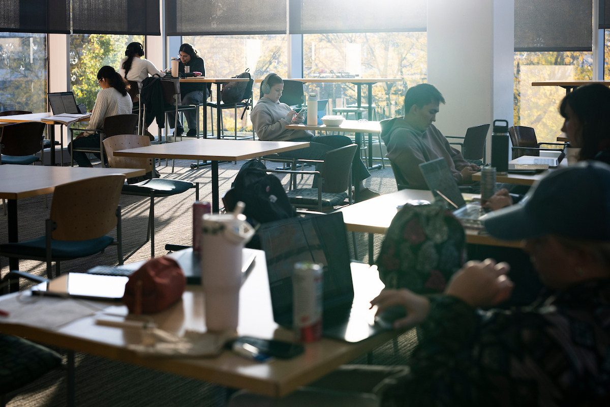 Students sitting at tables in a room with large glass windows